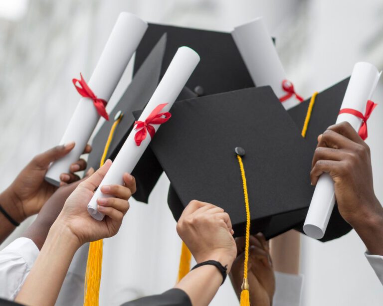 hands holding up graduation caps and diplomas